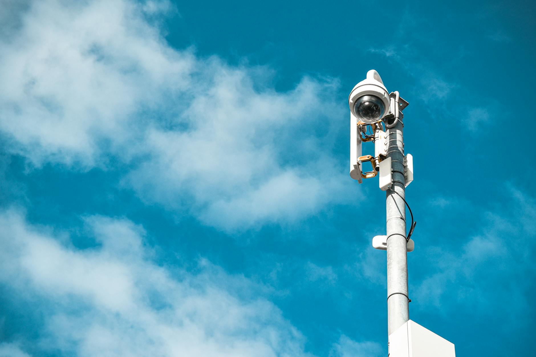 Zbliżenie na kamerę monitoringu zamontowaną na słupie na tle błękitnego nieba