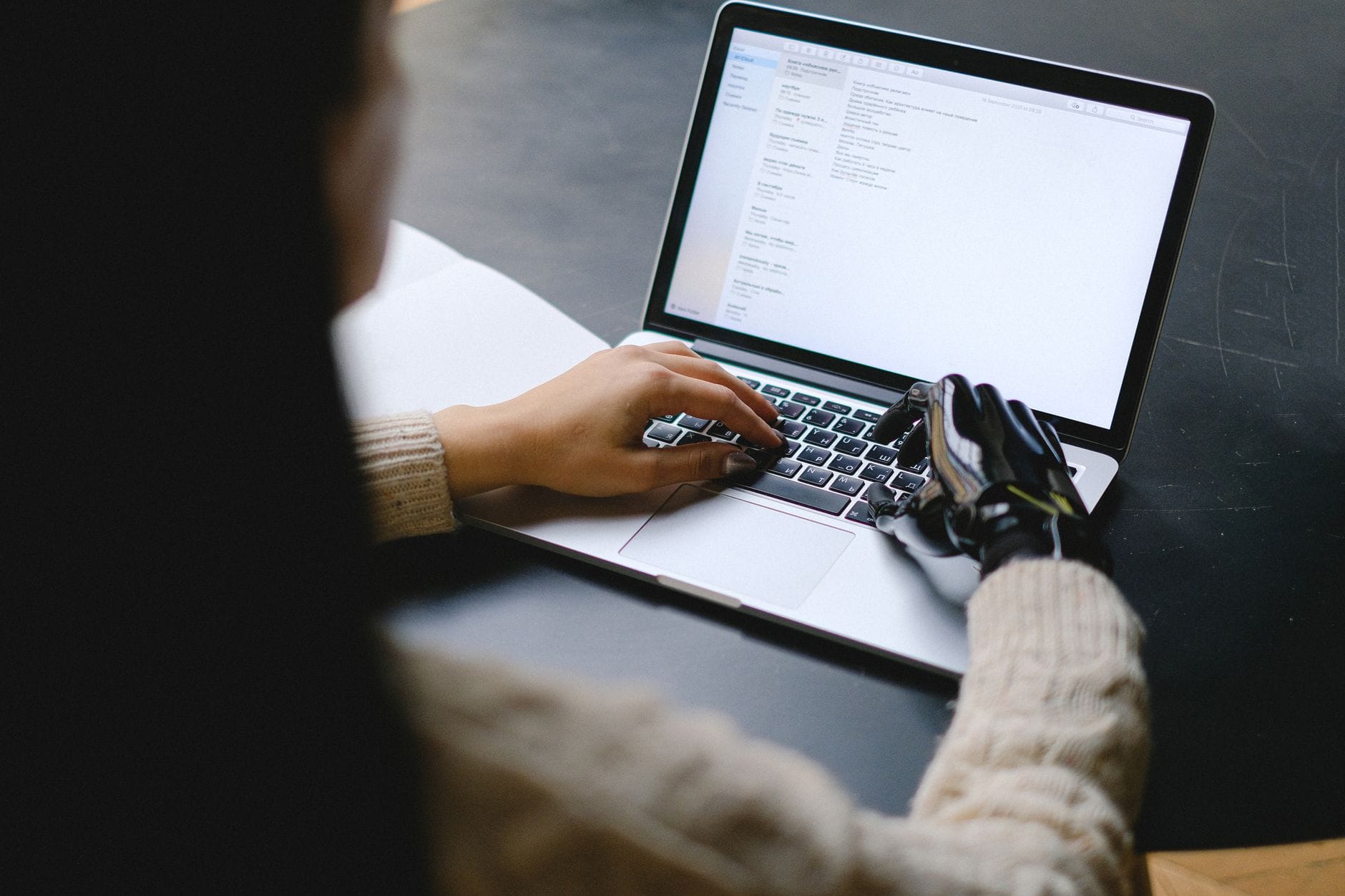 Osoba z protezą dłoni pracuje na laptopie w domu