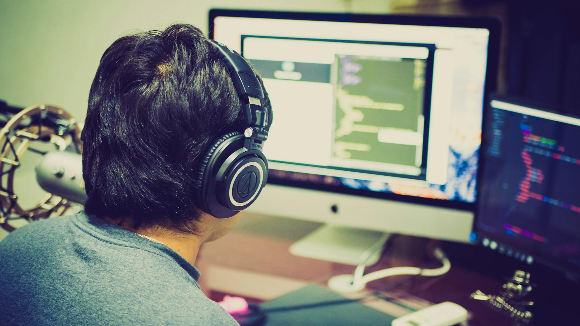 Programista w słuchawkach pracuje przy dwóch monitorach komputerowych