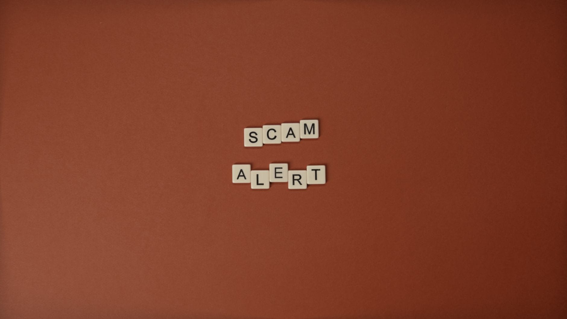 Kafle Scrabble układające się w napis Scam Alert na brązowym tle