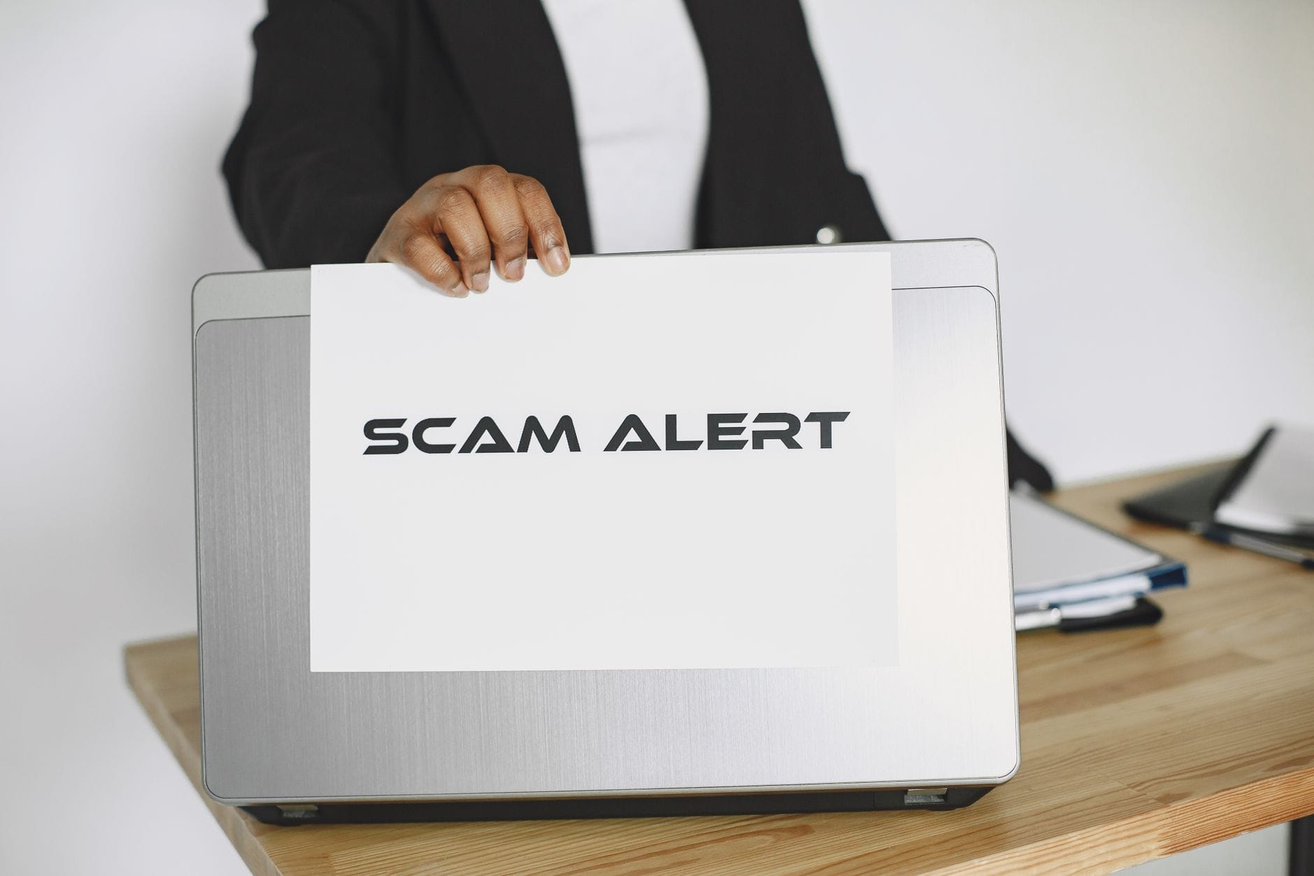 Pracownik trzyma kartkę scam alert nad laptopem jako ostrzeżenie przed BEC