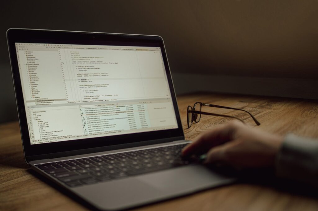 Osoba programująca na laptopie, okulary leżą na stole